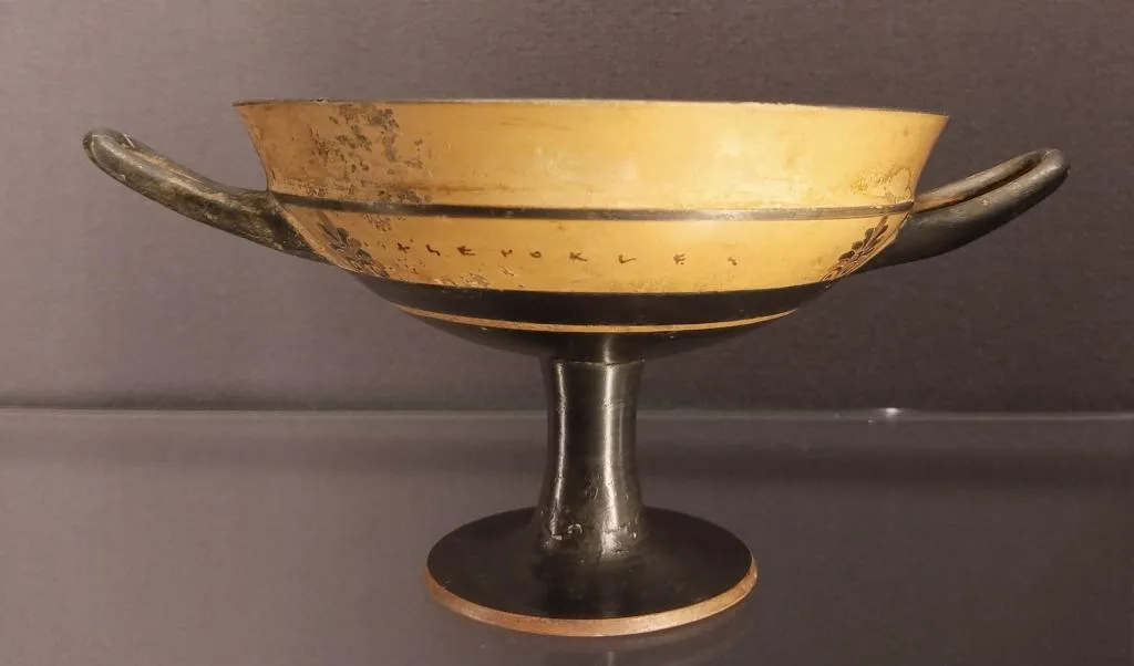 Ancient Attic band-cup kylix with two handles and a tall stem, featuring the potter’s inscription “Xenokles” around the rim. Dated ca. 540 BCE.