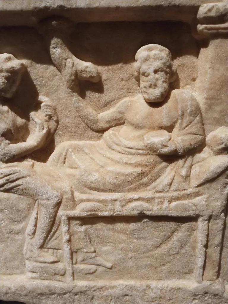 Carved marble relief showing a reclining male figure at a banquet, holding a rhyton missing its protome; Attic, late 4th century BC.