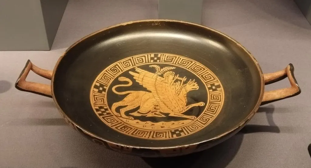 Ancient Greek red-figure kylix with two handles, depicting Apollo playing a lyre while riding a griffin, framed by a meander pattern. Attic, early 4th century BCE.