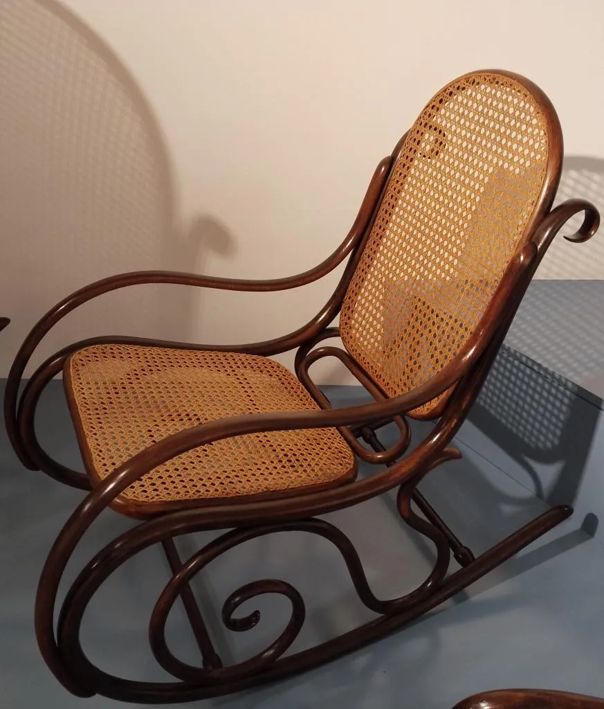 Photograph of a Thonet rocking chair with curved bentwood frame, cane backrest, and cane seat, demonstrating the company’s signature bentwood craftsmanship.