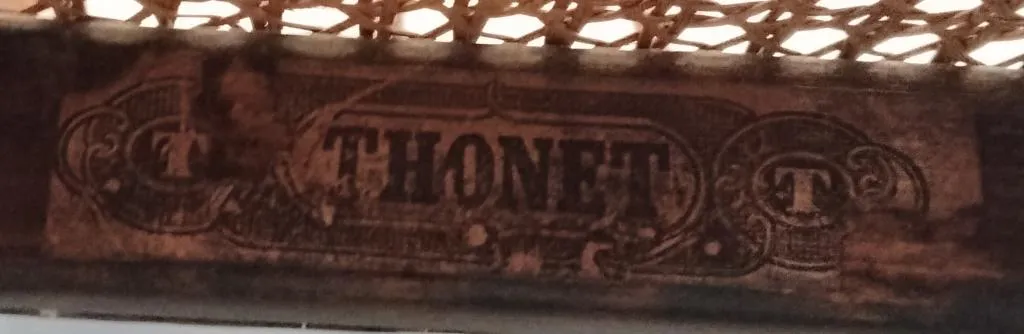 Close-up of a later Thonet paper label attached under a cane seat, showing the word THONET in bold print with ornamental T motifs on either side.