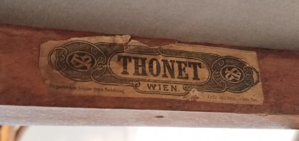 Close-up of a later Thonet paper label on a wooden chair frame, showing bold THONET WIEN in black print with decorative border.