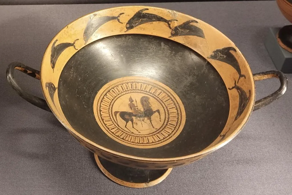 Antike ostgriechische Kylix mit zwei Henkeln. Innen: Tondo mit bewaffnetem Reiter, Rand mit springenden Delfinen verziert. Um 550 v. Chr.