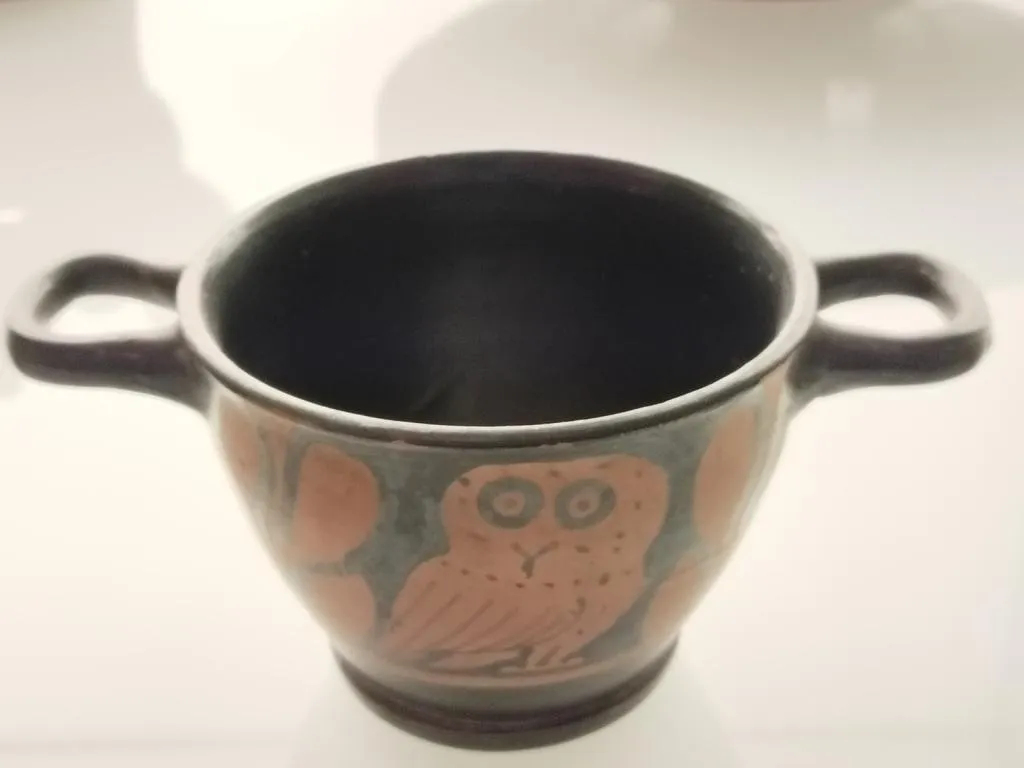 Two-handled ancient skyphos with a red-figure depiction of an owl and leaf motifs, Campanian style, black-glazed surface, 4th century BCE.