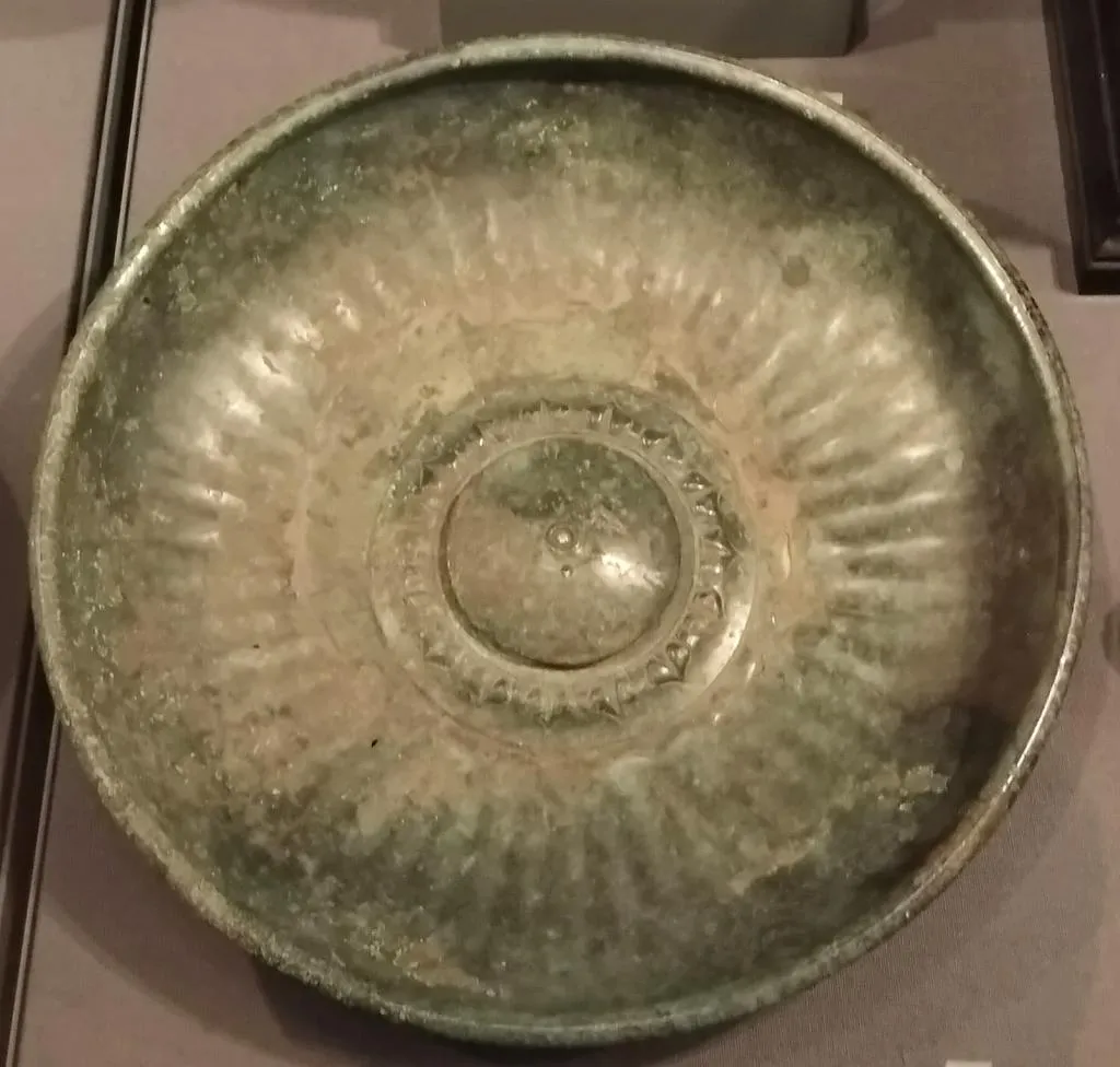 A greenish ancient Roman omphalos phiale with a central raised boss and radiating ribbed decoration, made in the early 1st century AD.