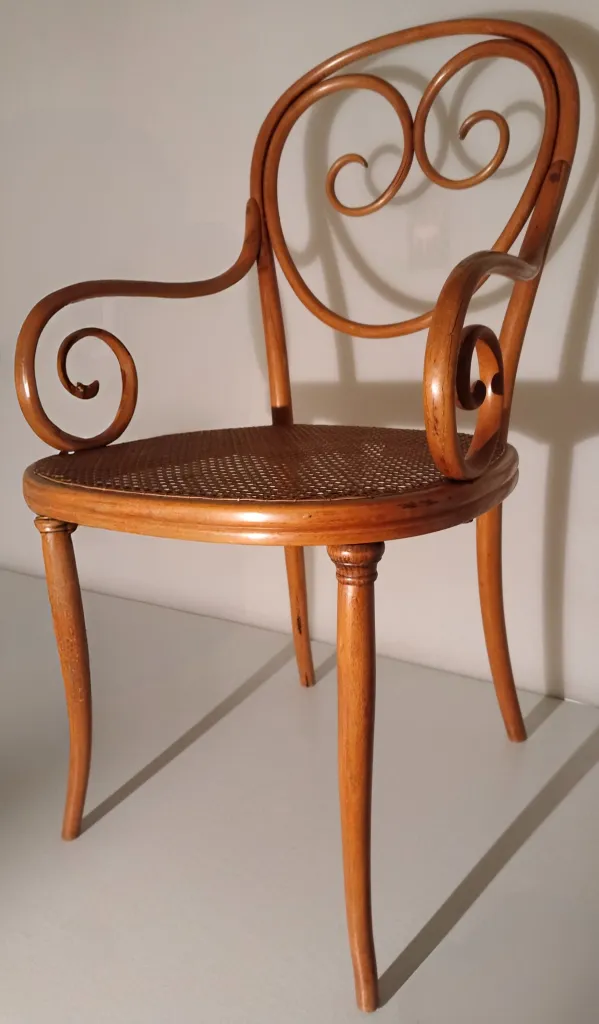 Side view of Thonet armchair model No. 2 with curved scroll armrests and woven cane seat.