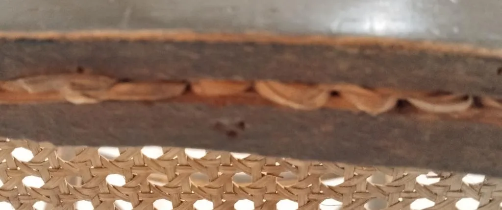 Close-up of three small embossed dots forming a triangle on the underside of a wooden Thonet chair frame beneath a cane seat.