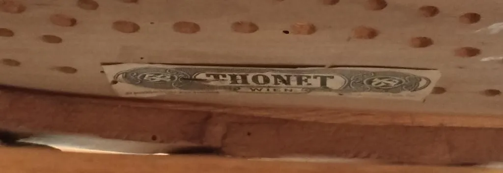 Close-up of a Thonet paper label on the underside of a wooden children’s swing cradle, showing THONET WIEN in bold letters with decorative framing.