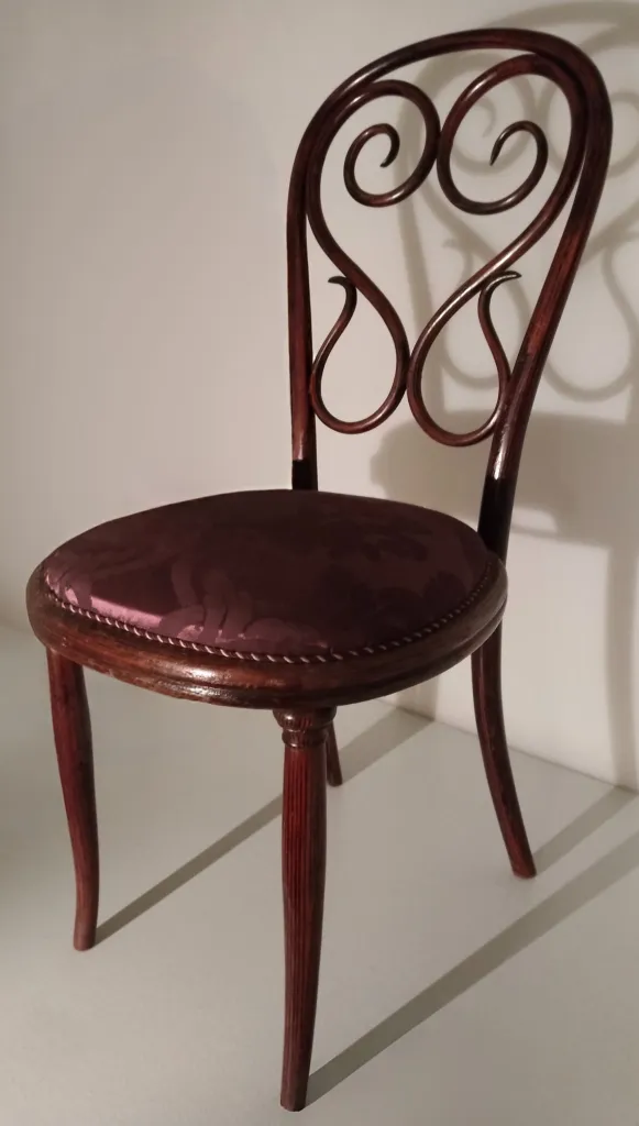 Seitenansicht des Thonet-Stuhls Modell Nr. 4 mit geschwungener Zier-Rückenlehne und gepolstertem Sitz.