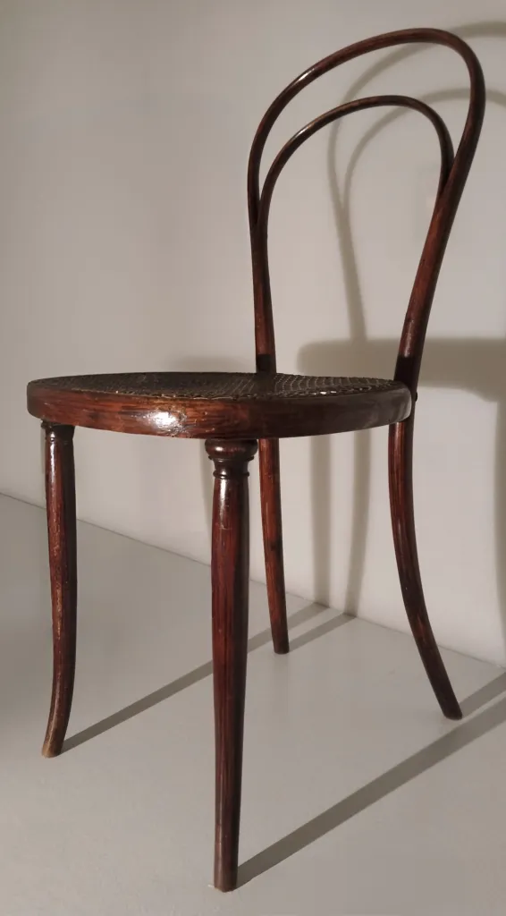 Seitenansicht des Thonet-Bugholzstuhls Modell Nr. 8 mit Rohrgeflechtsitz, gedrechselten Vorderbeinen und doppelt gebogener Rückenlehne aus dampfgebogenem Holz.