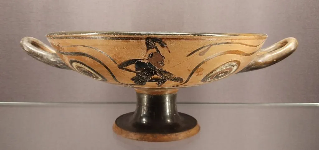 Ancient Greek eye kylix with black-figure decoration showing a helmeted warrior between painted eyes, dating to around 525 BCE.